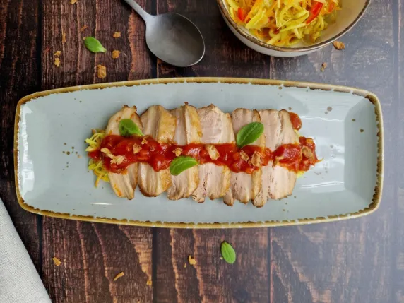 Buikspek gesneden op langwerpig bord met rode saus