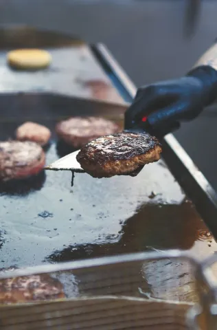 Kok bakt hamburgers op de grillplaat