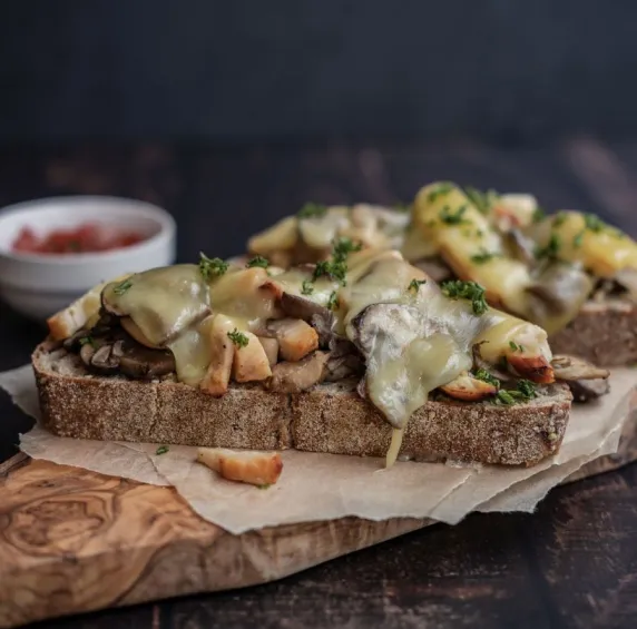 Houten plank met desembrood met paddenstoelen en gegratineerde kaas